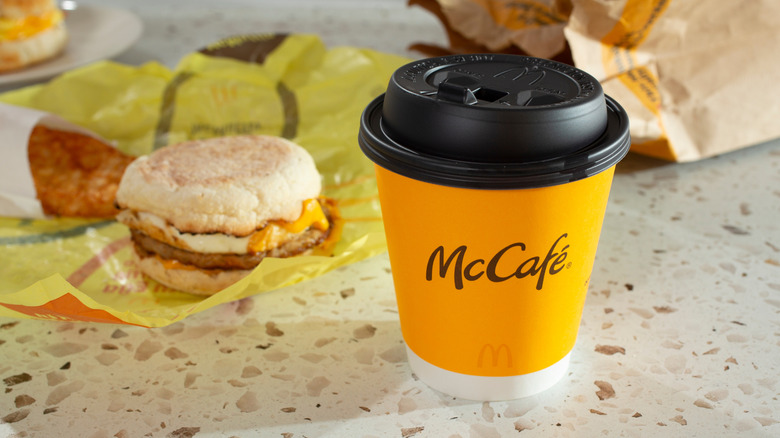 A breakfast sandwich Egg McMuffin sits behind a cup of coffee.