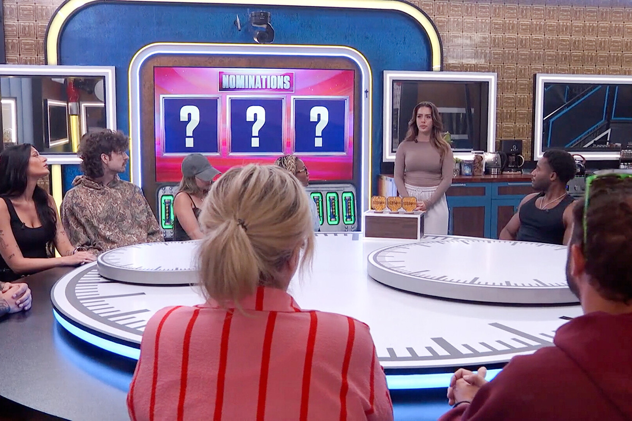 A group of people sitting around a circular table watch a woman standing in front of a screen that reads 