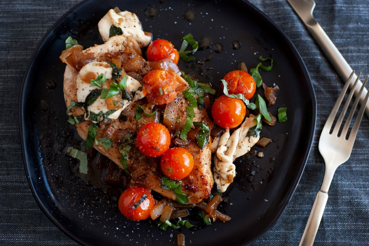 Chicken caprese on a black plate.