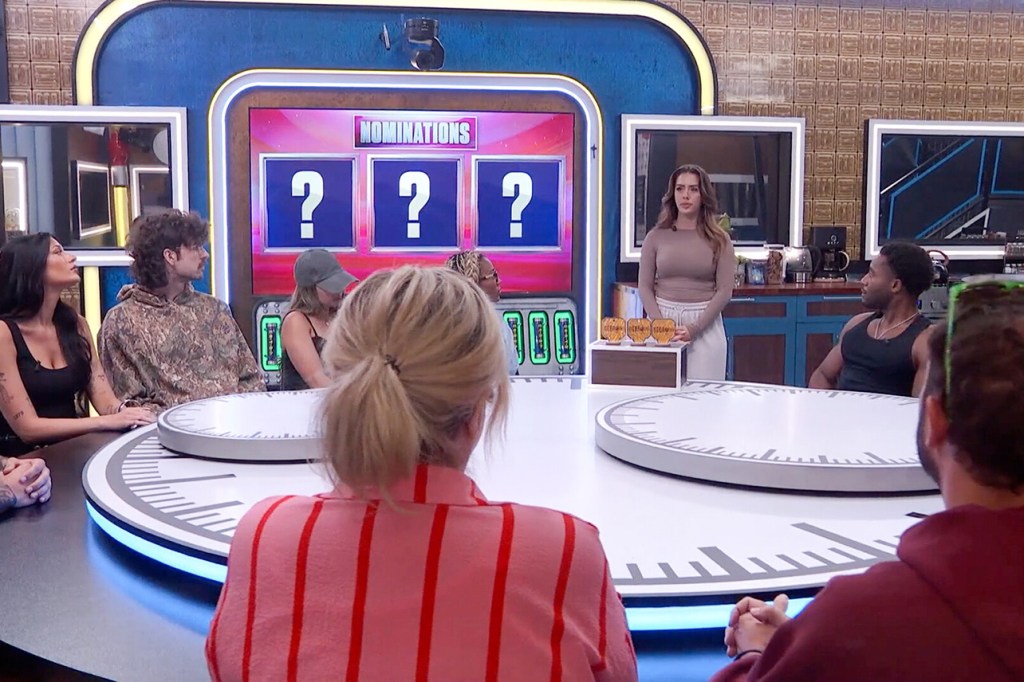 A group of people sitting around a circular table watch a woman standing in front of a screen that reads