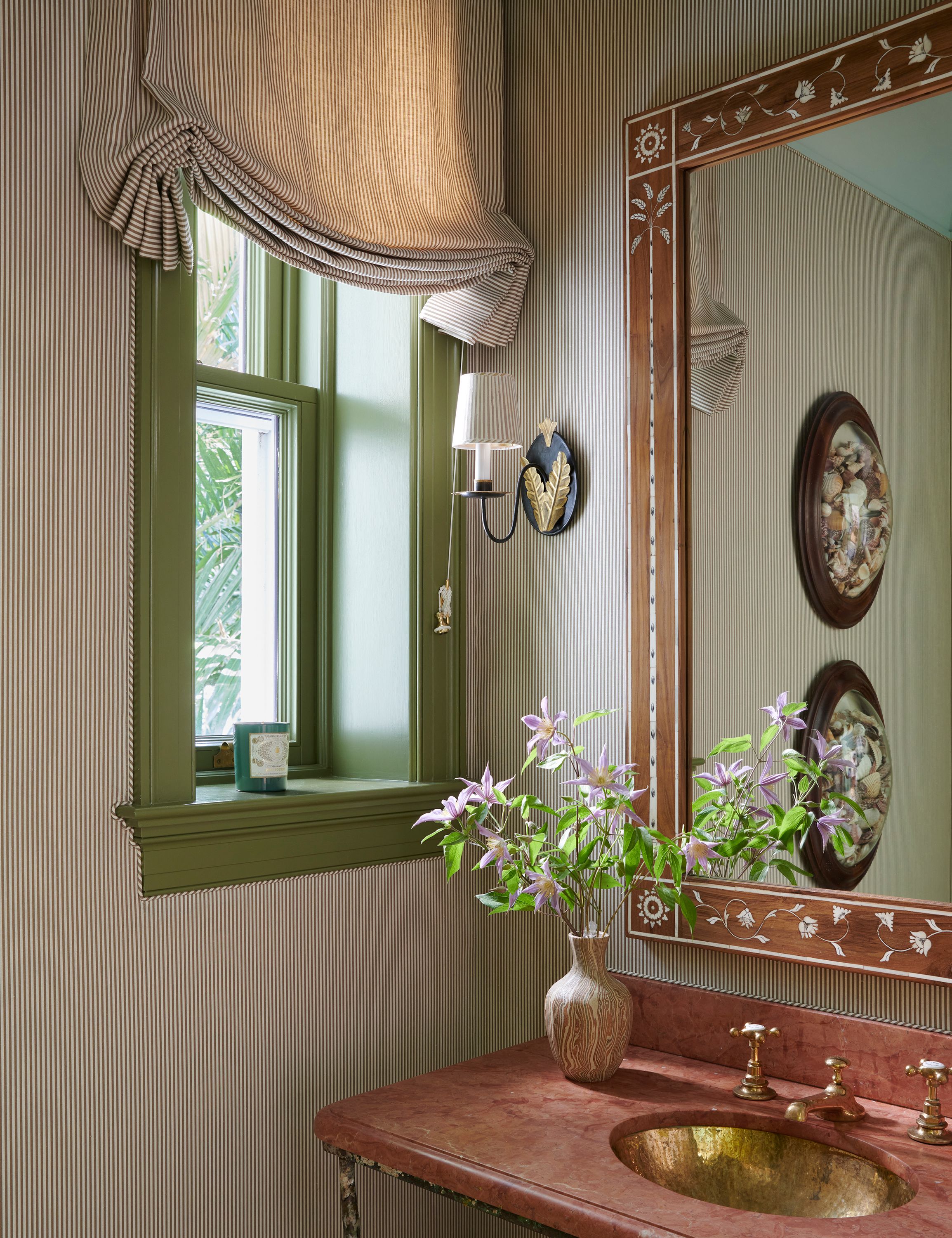 A mirror with mother-of-pearl inlay hangs above the washstand in another powder room. Piping in the same stripe as the walls and roman blinds wrap around the window frame, displaying the level of detail with which Graziolo and Kemble work.