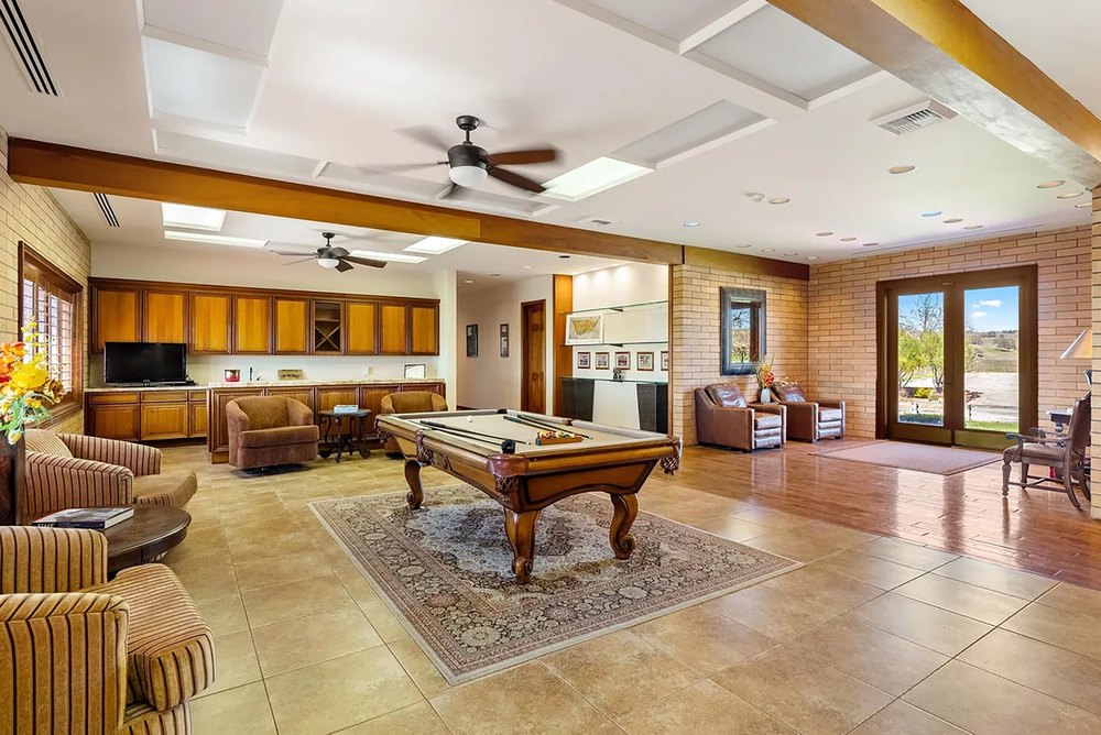 Spacious game room and lounge area featuring a central billiard table, wet bar, and exposed brick walls.