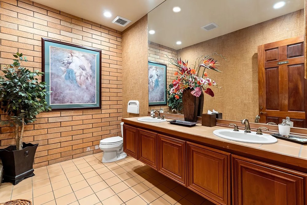 Bathroom featuring exposed brick accent walls, double vanity sinks, tile flooring, and warm lighting.