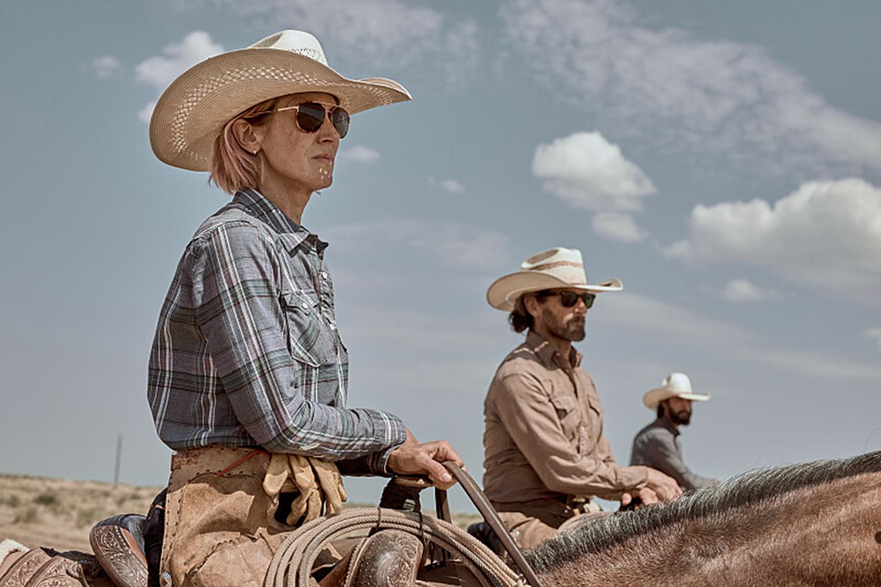 Three individuals on horseback wearing cowboy hats set in an open landscape under a cloudy sky