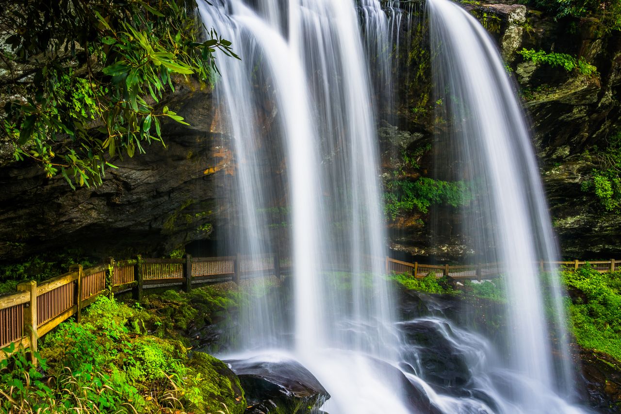 A waterfall flowing over a rocky ledge with a wooden walkway visible nearby