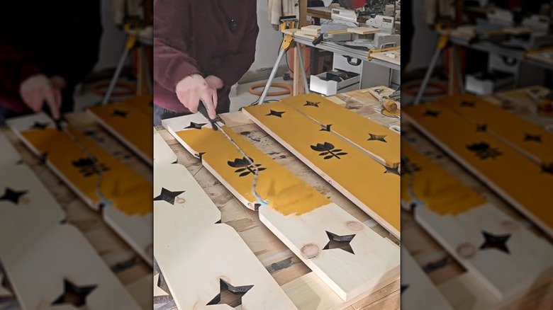 Woman painting wooden carved window shutters with yellow paint in DIY workshop