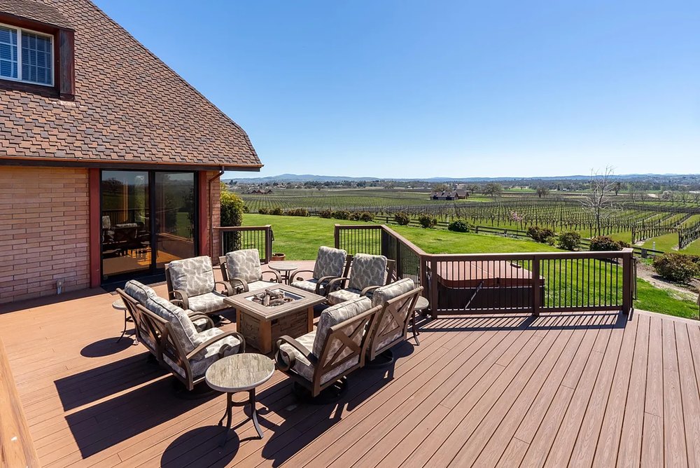 Spacious wooden sun deck with patio lounge seating and a fire pit overlooking vineyard landscapes.