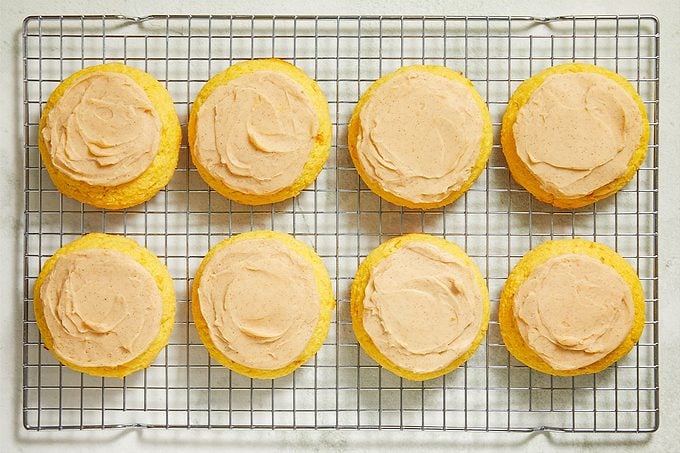 Overhead shot of frosted corn cookies arranged on a wire cooling rack, each topped with a smooth swirl of creamy frosting;