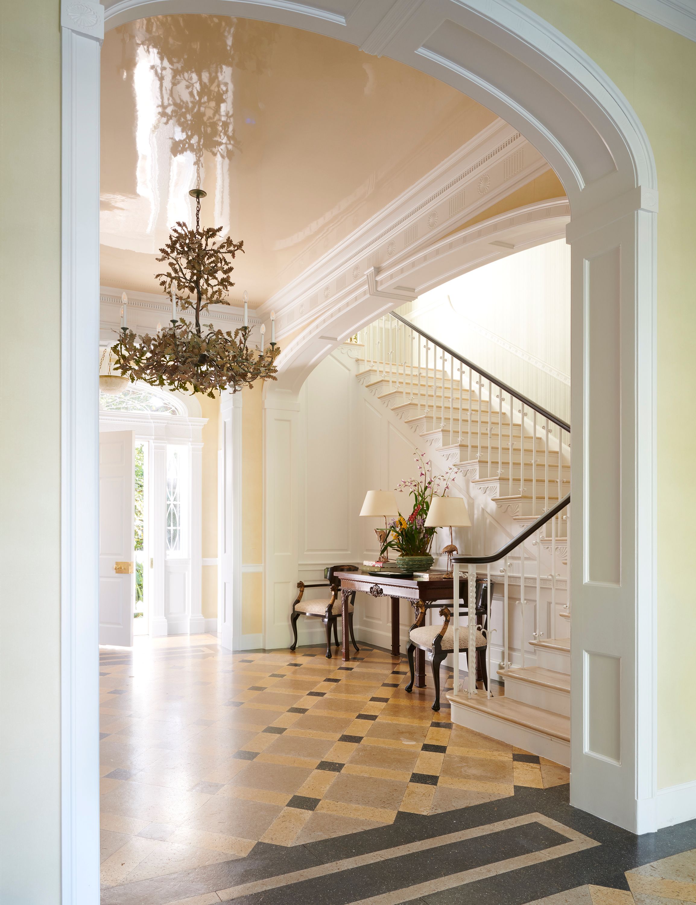 In the foyer, a high-gloss lacquered ceiling keeps the grand room fresh, while the checked composite floor underfoot beckons into the rest of the house. Antique side chairs and a console table, heirlooms from the wife’s father, decorate the alcove underneath the home’s original stairs.