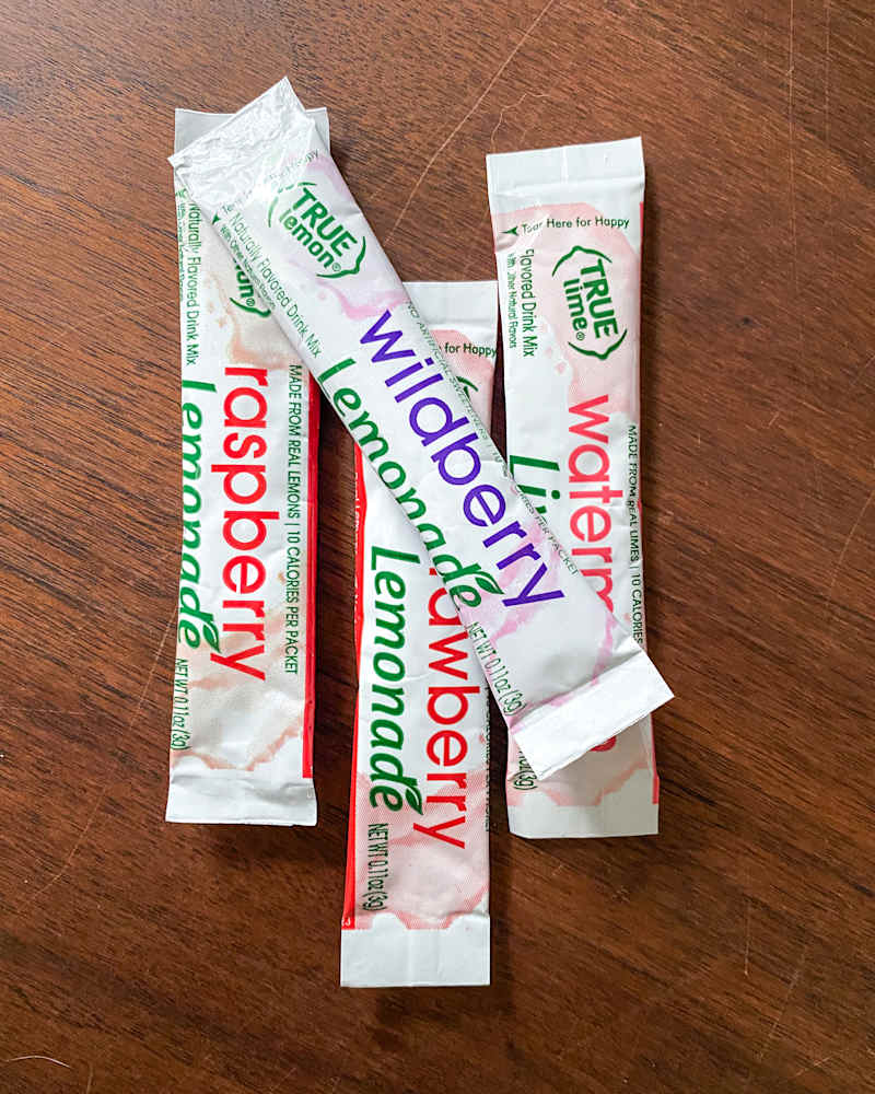Four drink mix packets labeled raspberry lemonade, wildberry lemonade, and watermelon lemonade on a wooden surface.