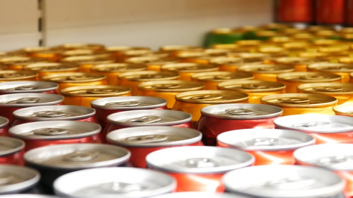 A line of cans sit in a refrigerator.