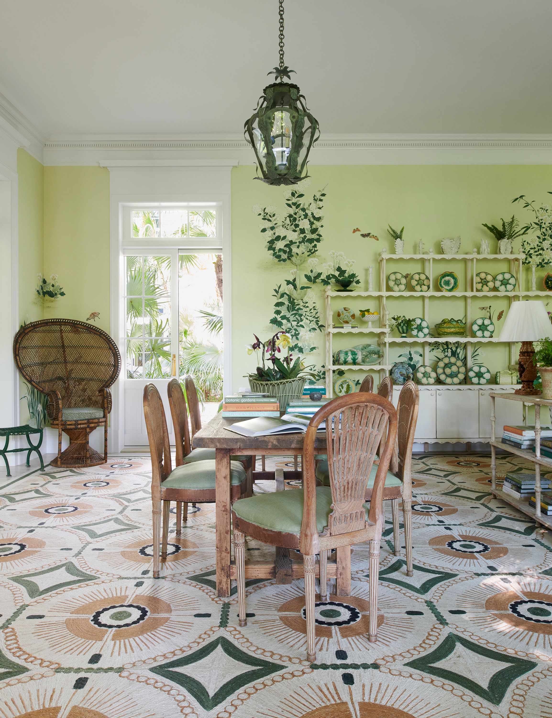 The family room works well for casual meals and entertaining, courtesy of a farmhouse table and antique French carved wooden chairs. A Patterson Flynn rug gives the impression of floor tiles. The lantern is from Vaughan Lighting. The wallpaper is custom from De Gournay.