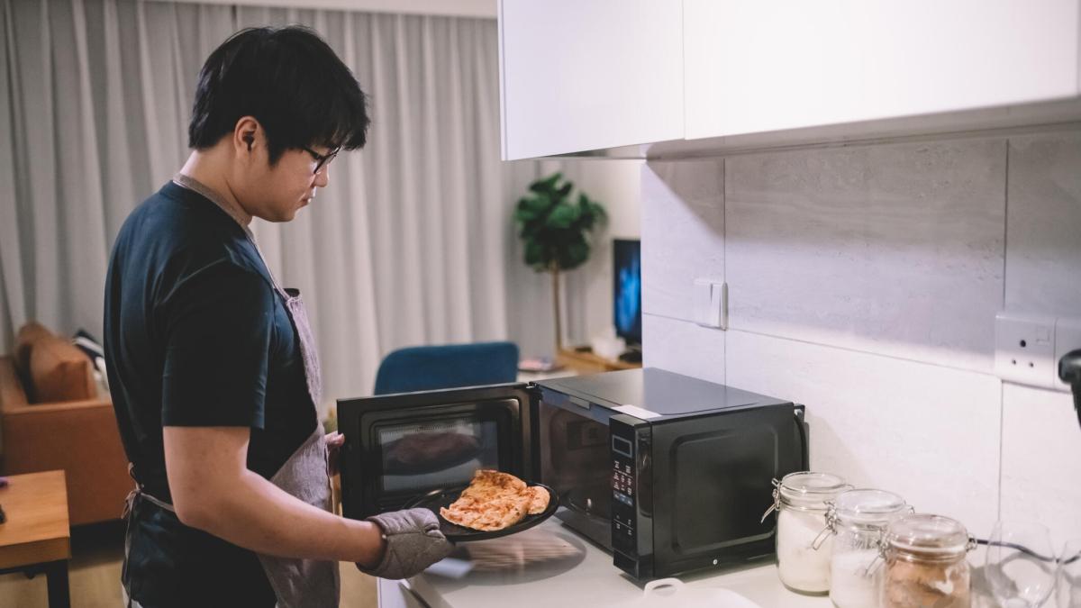 A person putting pizza slices on a black plate into a black microwave.