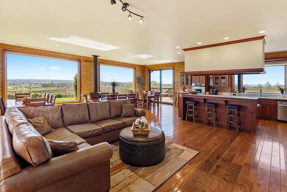 Open-concept living and dining area featuring leather sofas, wood floors, and panoramic landscape windows.