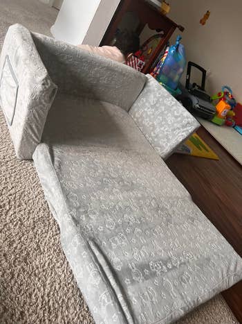A children's fold-out sofa with playful patterns in a playroom, surrounded by toys and a child partially visible behind it