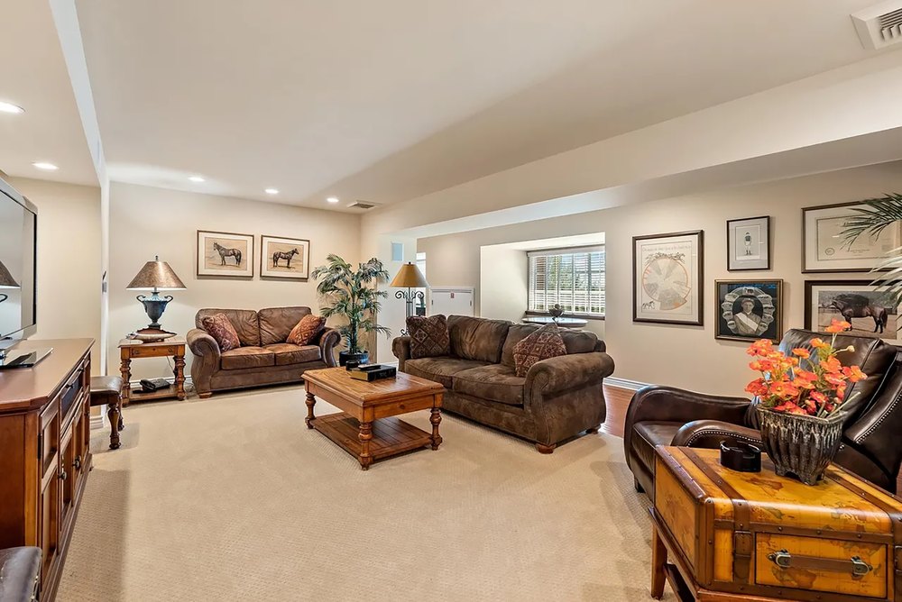 Spacious living room featuring plush leather seating, wall art, neutral carpeting, and warm lighting.