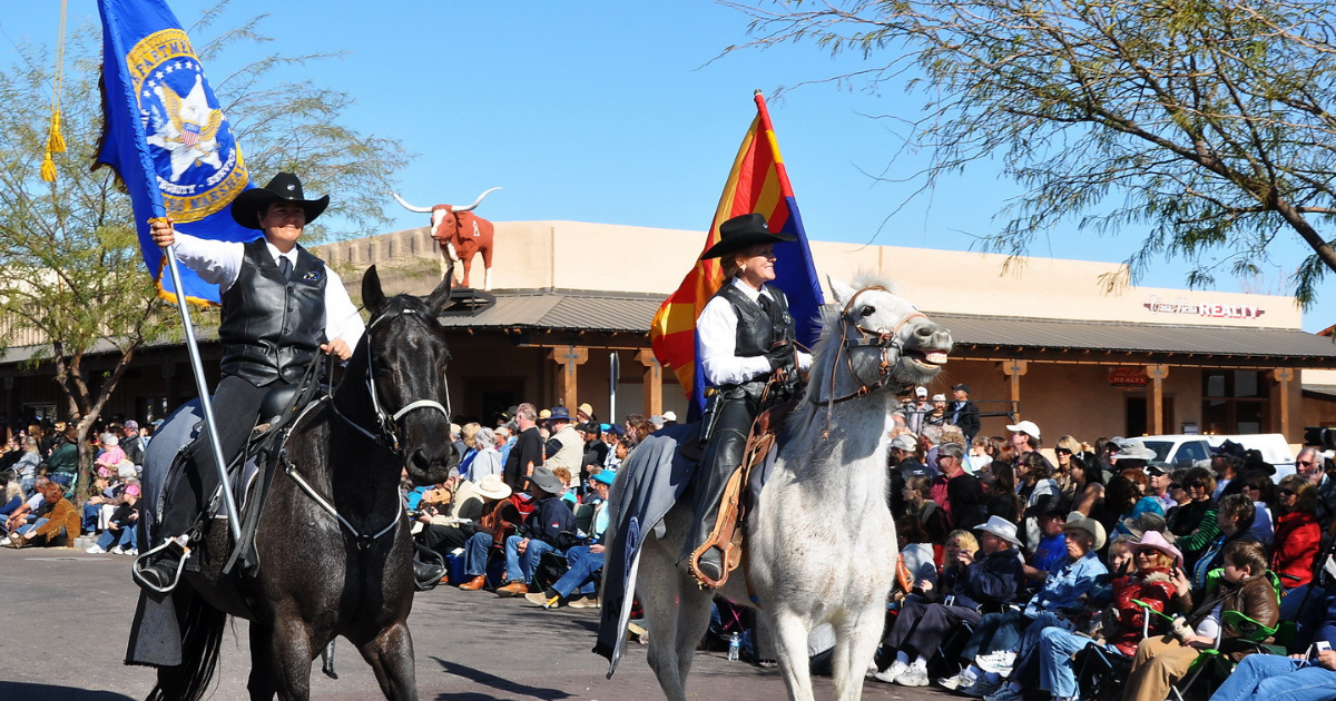 Horseback riders carry flags during the Gold Rush Days parade in downtown Wickenburg, Arizona, with spectators lining the street.