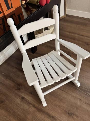 Wooden rocking chair with slatted seat and backrest, positioned indoors on a wooden floor