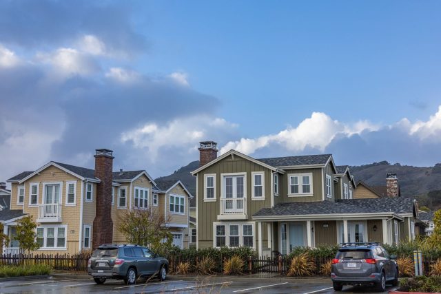 Picturesque suburban neighborhood with modern houses and parked cars under a partly cloudy sky.