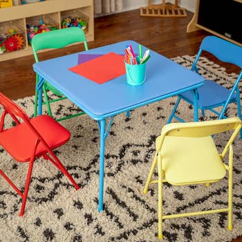 Children's playroom table set with blue table, red and yellow chairs, and crafting supplies on a patterned rug