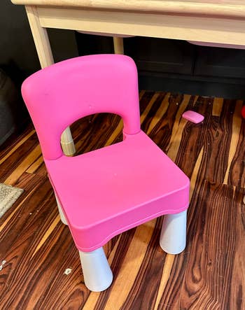 Children's pink plastic chair with sturdy legs, placed on a wooden floor next to a table