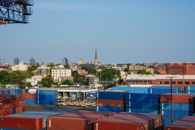 Shipping containers stacked in a port with city skyline.