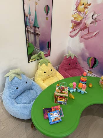 Kids' playroom with plush fruit-shaped chairs and a green table, featuring toys and books for interactive play
