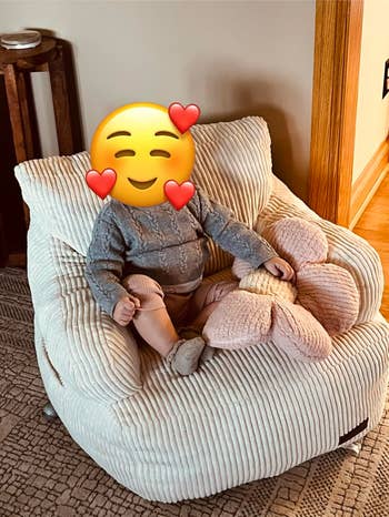 A baby sits in a soft chair with a plush toy