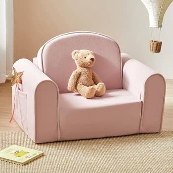 Children's plush armchair with a teddy bear sitting on it, a star wand in the side pocket, and a book on the floor nearby