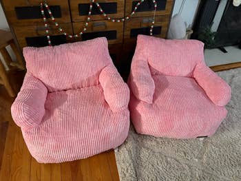 Two pink corduroy armchairs are placed side by side in a cozy living room setting with wooden floors and a decorative chest