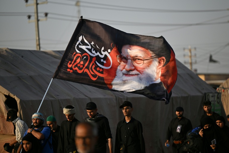 Shiite Muslim pilgrims hold a flag bearing the portrait of Iran's slain supreme leader Ayatollah Ali Khamenei as they march to the Iraqi city of Karbala