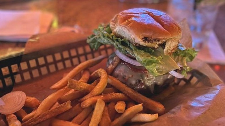 Massive burger with lettuce, cheese, and onion in tray with fries