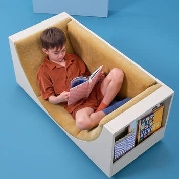 Child sitting in a modern chair with built-in storage, reading a book. The chair is designed for comfort and compact living spaces