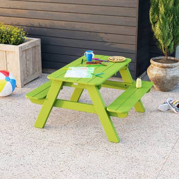Children's picnic table on a patio, with craft supplies and snacks, next to a planter and a beach ball