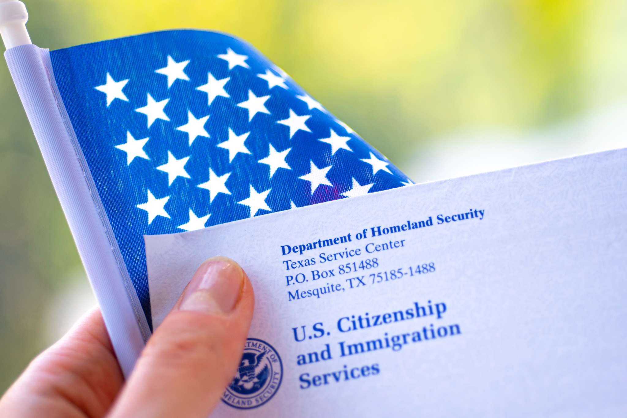 Stock image: Letter from USCIS and flag of USA in hand on green blurred background (Washington, DC, USA – September, 16, 2019).