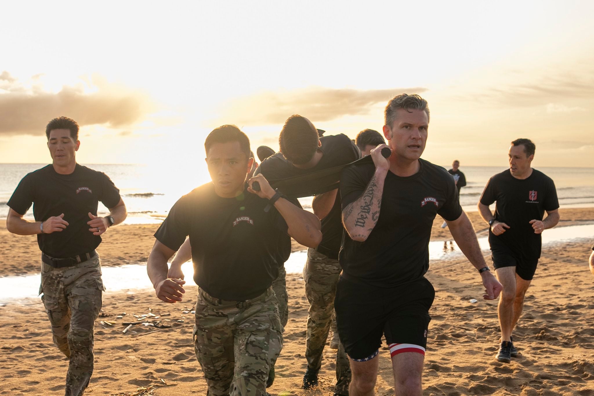 Pete Hegseth helps carry a soldier on a stretcher while running on a beach as part of a training exercise. / Pete Hegseth/X