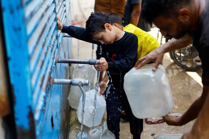 Palestinians fill jerrycans with water at a water distribution point, in Nuseirat