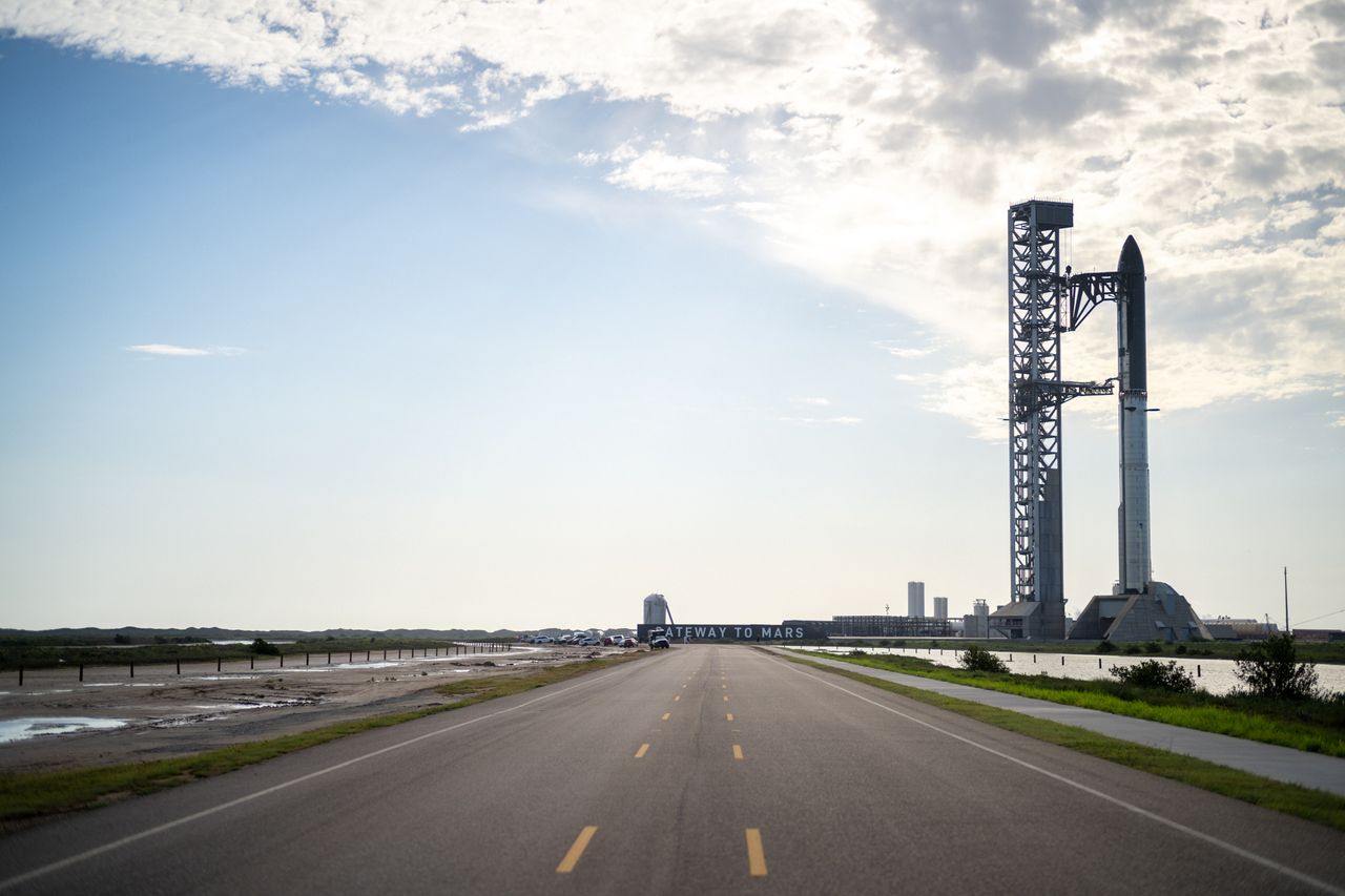 A SpaceX Starship docked at a launch pad in Boca Chica Beach, Texas against a blue sky with few clouds.