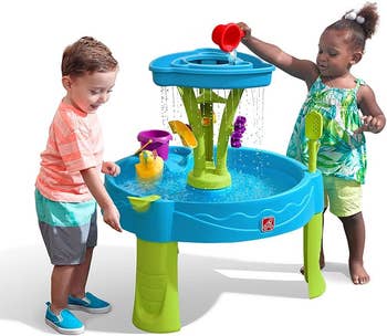 Two children playing with a water activity table, pouring water and interacting with floating toys. Great for outdoor fun