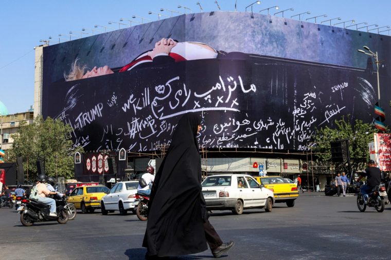 TOPSHOT - A woman crosses Tehran's Enghelab Square on July 15, 2026, past a giant anti-US billboard featuring US president Donald Trump in a coffin with text in Persian reading