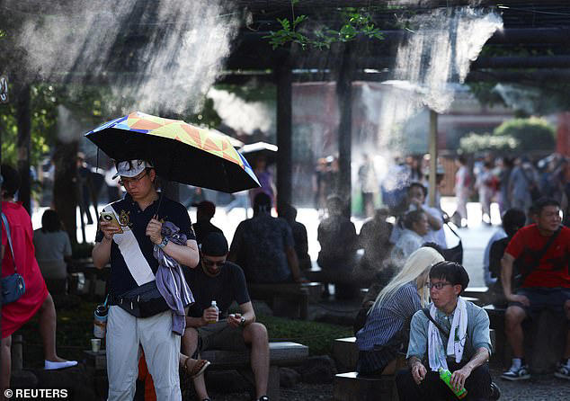 This comes as Japan faces a heatwave that has sent temperatures soaring to 38°C (100°F), sending 4,500 people to hospital with heatstroke symptoms. Pictured: People in Tokyo seek shelter under a cooling mist 