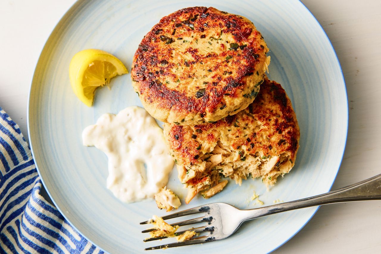 Two tuna patties on a plate with a lemon wedge sauce and a fork