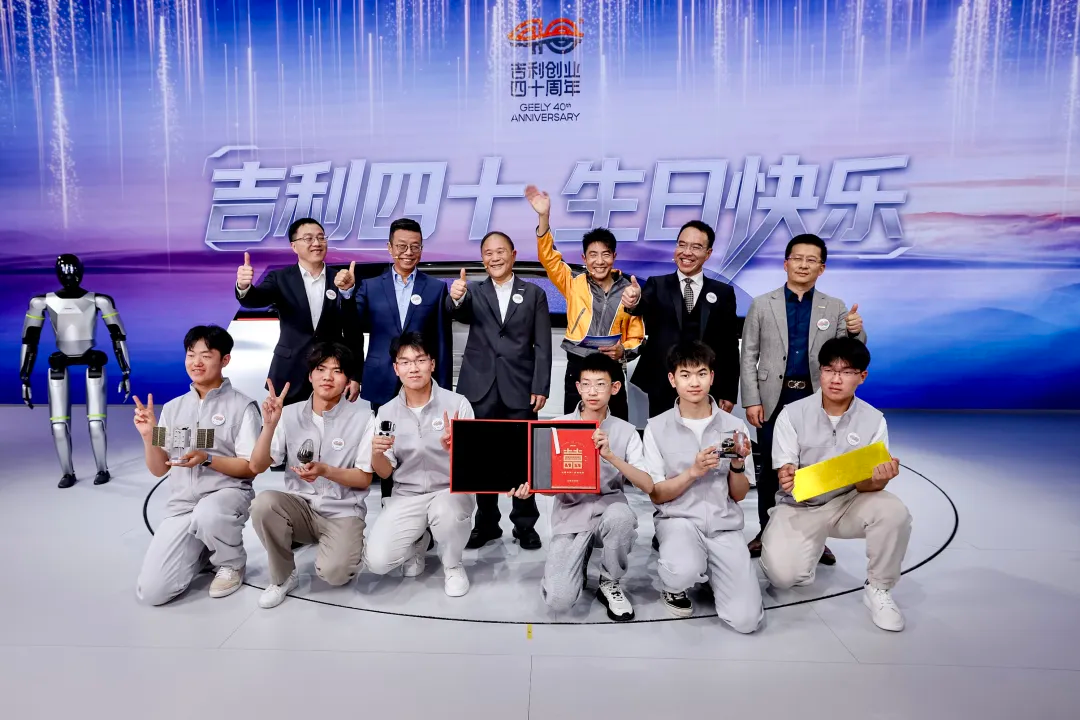A group of people celebrates Geely's 40th anniversary, posing with awards and a robot in the background