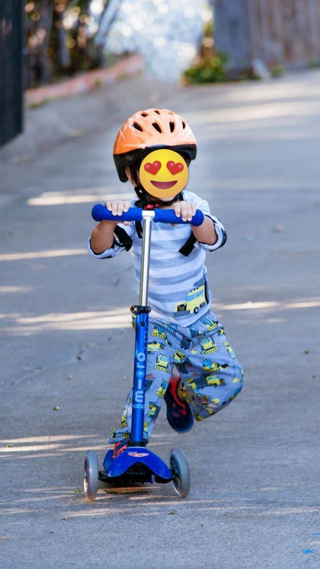 Child in patterned pants and striped shirt riding a scooter with a helmet