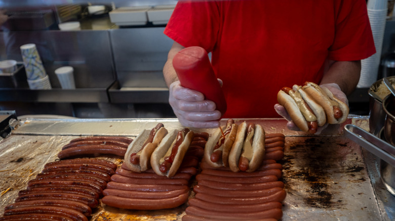 Nathan's Famous employee grilling hot dogs on flat top and dressing them with ketchup