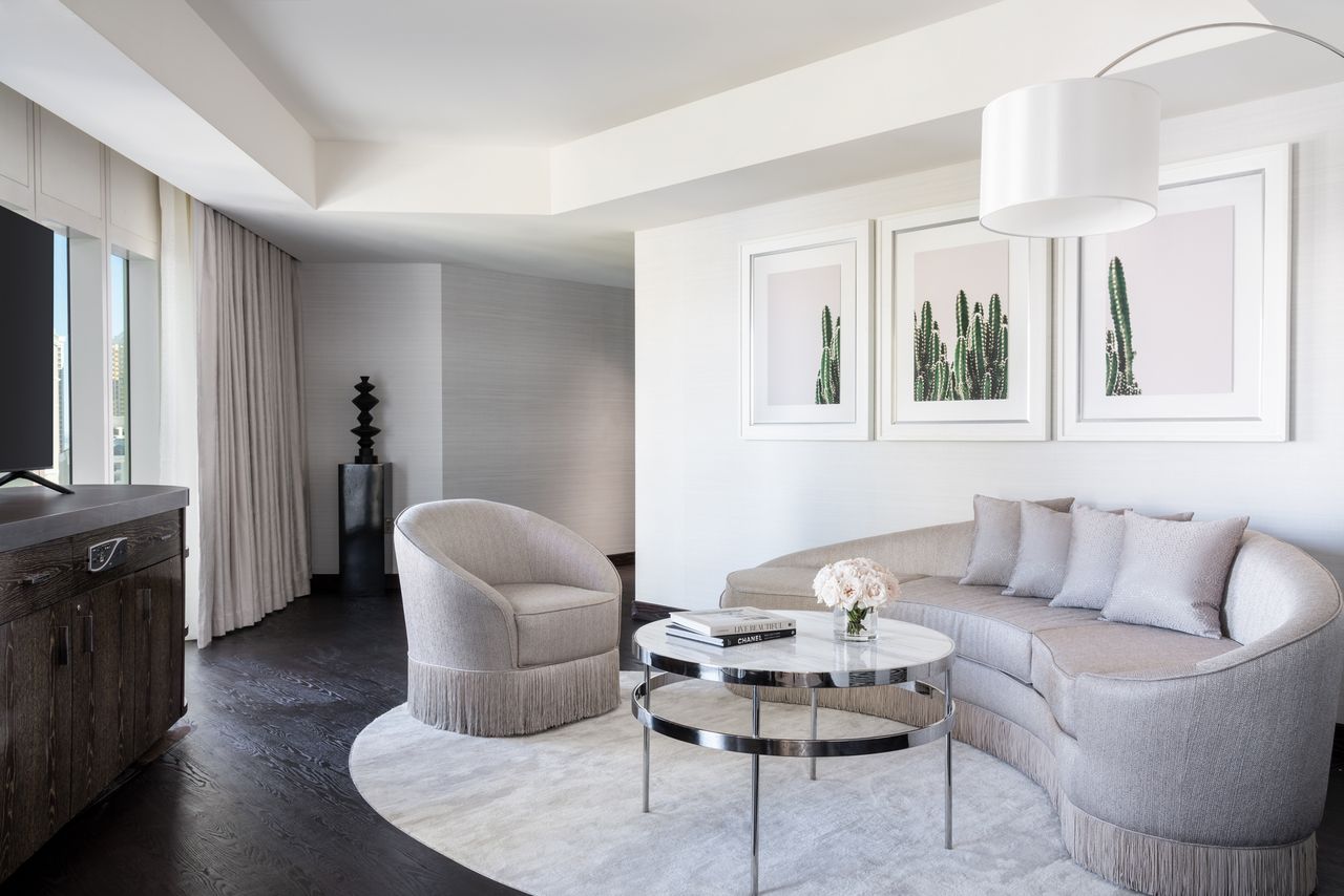 Modern living room with a curved sofa glass coffee table framed cactus art and a view towards a minimalist corner