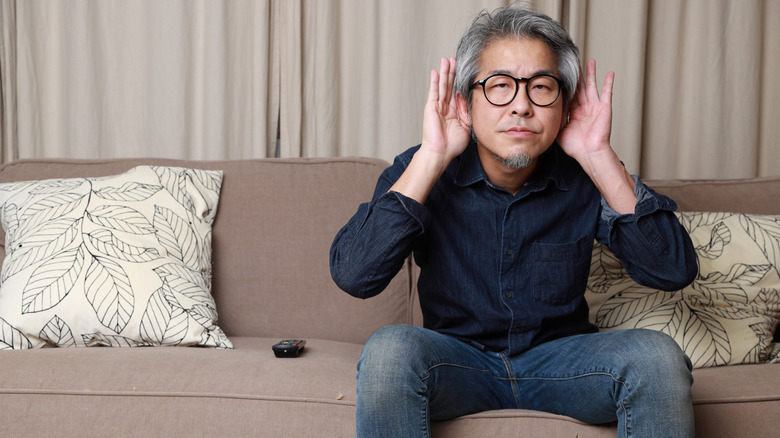 Man sitting on couch with hands to ears indicating trouble hearing