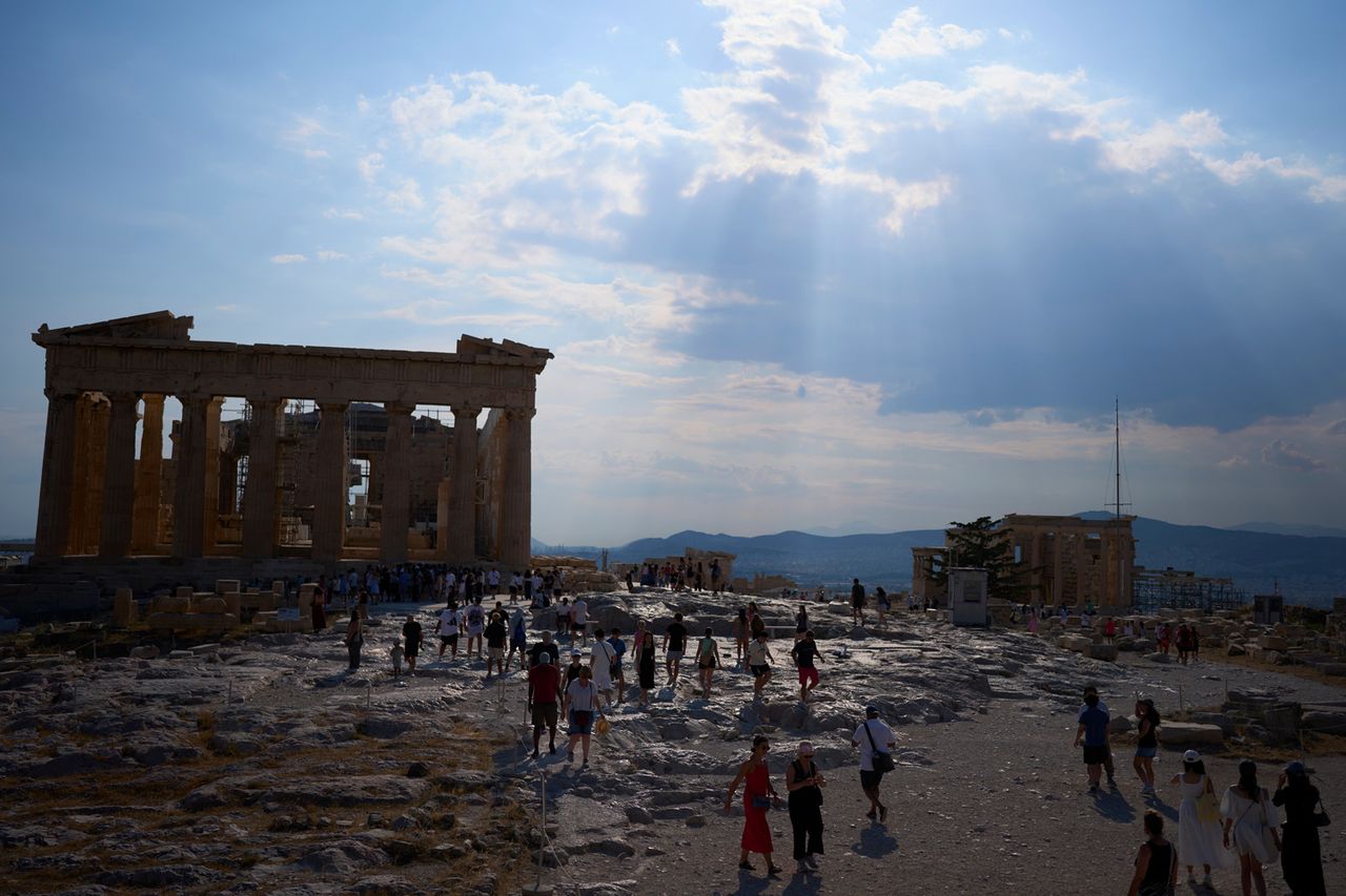 - Sun rays break through the clouds above the ancient Parthenon temple as tourists walk across the Acropolis during a hot day in Athens