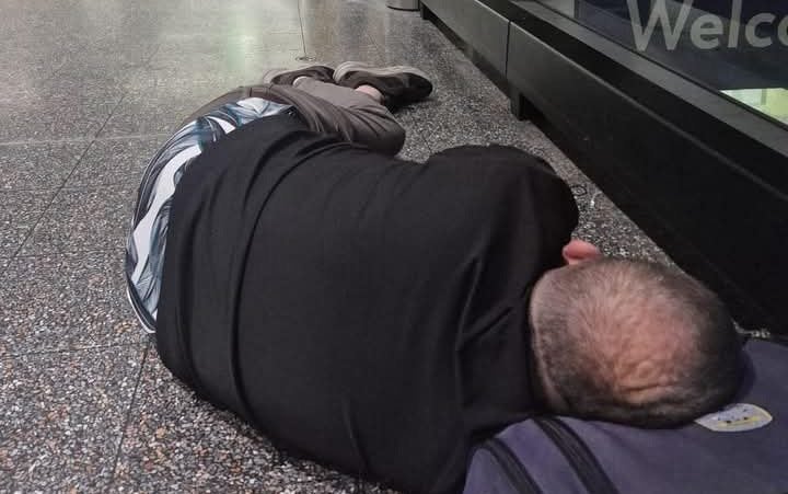 Wayne Lawson sleeping on the floor using his bag as a pillow in Gatwick Airport