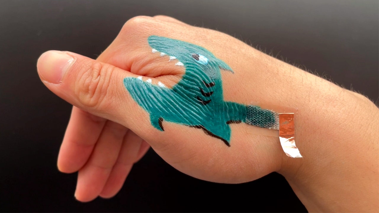 A hand with a painted shark tattoo.